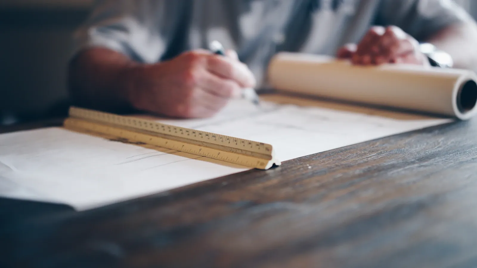 A person working on a large architectural drawing at a wooden desk