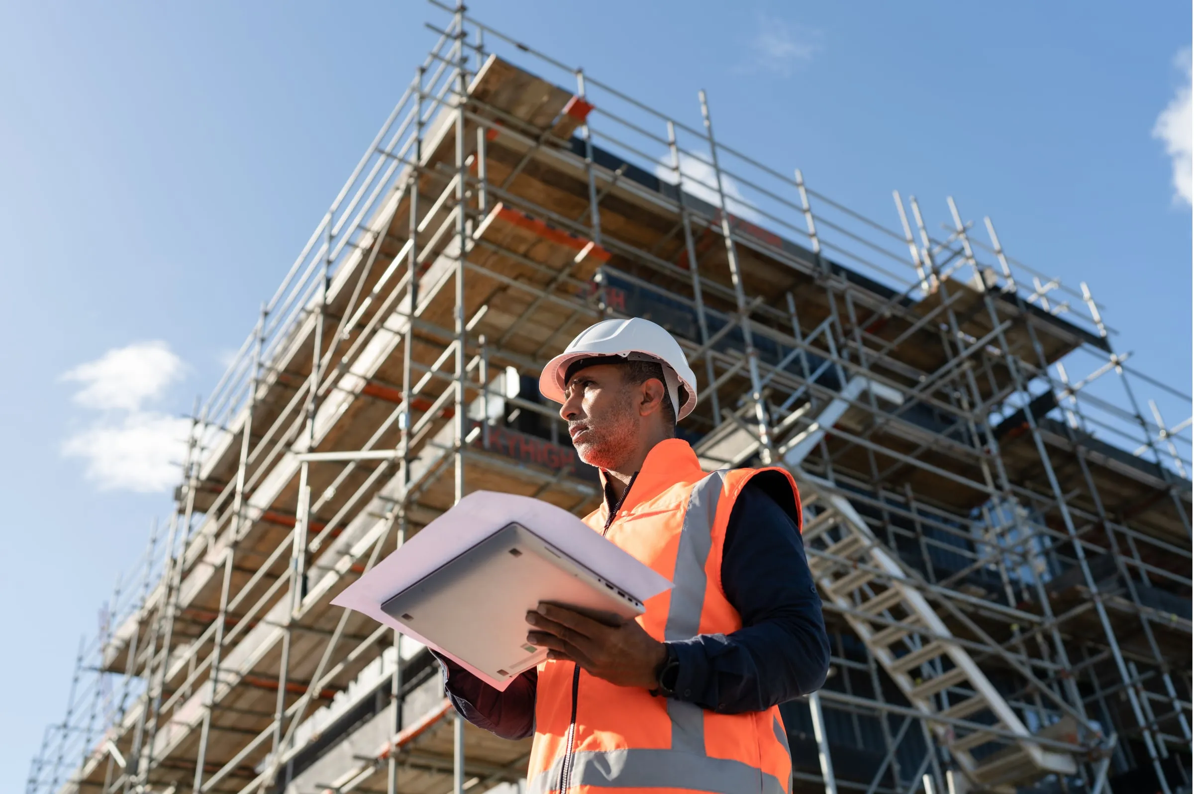 Surveyor in safety equipment holding plans at a construction site